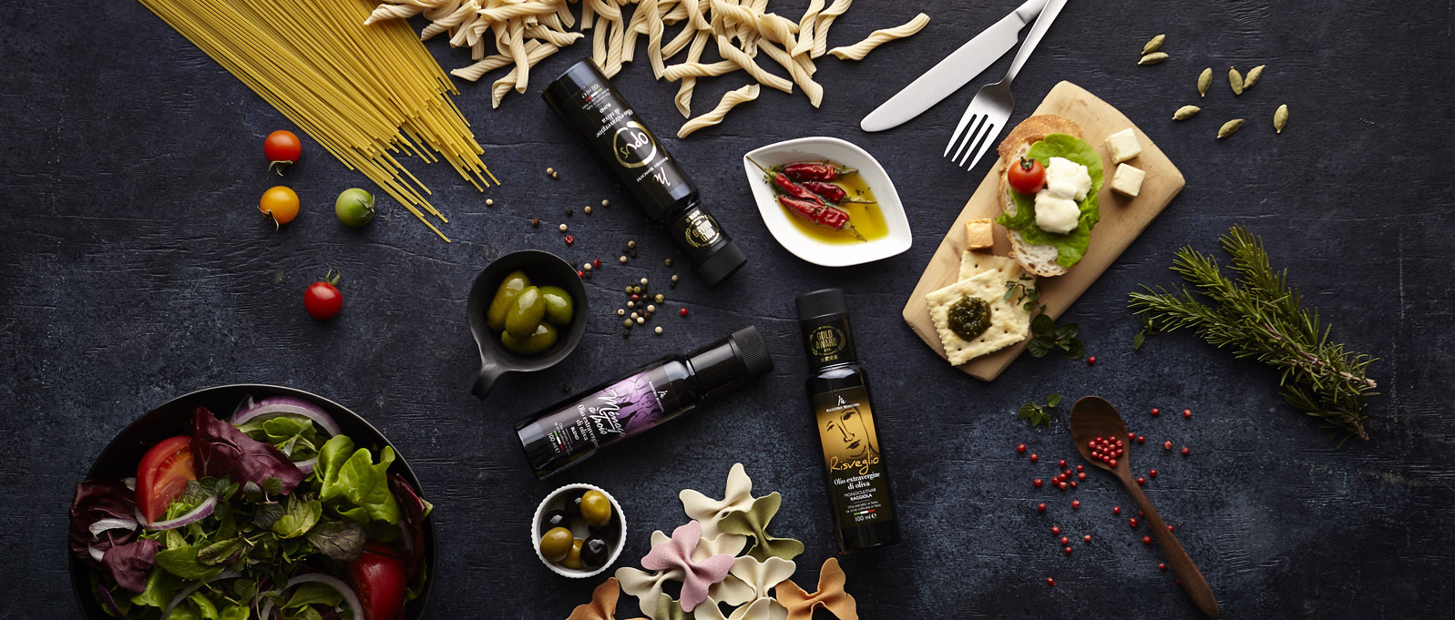 Gli oli Emozioneolio Opus, Ménage à Trois e Risveglio accanto a pasta, insalata, olive e bruschette
